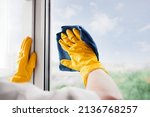 Small photo of Man in yellow rubber gloves cleaning window glass with cleaner spray detergent and squeegee or rag at home, office, copy space. Housework and housekeeping, home hygiene. Blue sky view, plastic windo