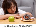 Small photo of Young beautiful, chubby women choose donut rather than an apple. which can cause overweight or health problem Junk food that can cause obesity and unhealthy for human body.