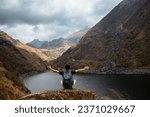 Small photo of A tourist with a backpack sitting with open arms on a rock on the shores of a lagoon (Laguna Linda, Pachitea, Peru), peace, concept of traveling, tourism