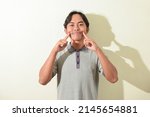 Small photo of asian man facial expression forced, contrived, fake smile. portrait of indonesian man in gray t-shirt on white background isolated