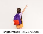 Small photo of A child with a satchel points with his index finger at your advertisement on a white isolated background. Preparatory summer courses for children.