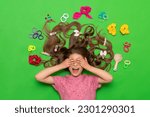 Small photo of Hair accessories. A happy little girl lies surrounded by elastic bands and hair clips, and covers her eyes with her hands, smiling broadly. Hairstyles for children. Green isolated background.