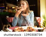 Funny blonde girl in jeans jacket eating pizza at restaurant.
