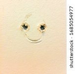 Small photo of A picture frame and drywall screw anchors form a happy face in the wall. An encouraging nudge for a do it yourself carpenter or home decorator.