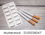 Small photo of A blister pack with nicotine gum and three cigarettes on a wooden background as a symbol of smoking cessation