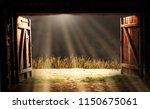 View from an open door of an old wooden barn. The sun shines through the storm clouds. Before the barn there is a corn field.