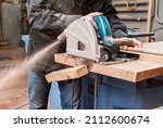 Male carpenter sawing a board with a circular saw in a carpentry workshop close-up