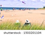 back of a couple wearing fishing sun hats sitting in lawn chairs behind tall green grass at the beach relaxing with people and kites in the background at Presque Isle State Park
