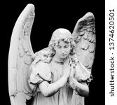 Small photo of Guardian angel sculpture with open wings isolated on black background. Angel sad expression sculpture with eyes down and hands together in front of chest. BW photog. Non-modern religious statue.