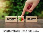female hand touching a wooden cube with arrow icon between the options of accept or reject. The decision or choice between accepting or rejecting. 