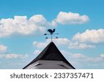 Small photo of compass symbol with sky, The rooster-shaped weather vane rises against the blue sky, Old country weathercock vane with compass arrow on a tiled roof, wind direction indicator, summer day.