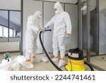 Small photo of Operators in type 5-6 hazmat suits mutually performing decontamination procedure with high efficiency vacuum cleaner, after asbestos incident