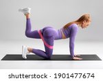 Fitness woman doing kickback exercise for glutes with resistance band on gray background. Athletic girl working out donkey kicks