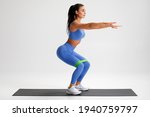 Fitness woman doing squats exercise for glute with resistance band on gray background. Athletic girl working out