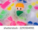 Small photo of Washing of children toys, plastic building blocks with figurines. A smiling little fellow and colorful cubes float in the foaming water