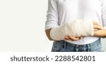 Small photo of Close-up of a woman's broken arm in a cast. The girl holds a bent arm against the background of a white T-shirt. Appropriate treatment in Western medicine.