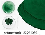 Small photo of Spirulina face mask or cream. In a Petri dish. Spirulina diluted in water in a Petri dish. Spirulina powder close-up. On a light background. View from above.
