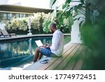Skilled businessman using mockup laptop for making online ticketing and banking during resort recreation on Bali island, Middle Eastern digital nomad connecting to villa wifi on blank netbook