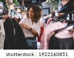 Smiling female standing near hangers with brand wear and laughing during Black Friday shopping with discounts, funny hipster girl enjoying pastime for update her wardrobe spending day in boutique