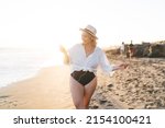 Carefree female tourist in swimsuit enjoying positive music during summer vacations on Tahiti using internet connection at seashore, smiling Caucasian woman in earphones listening audio playlist
