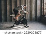 Small photo of Side view of male athlete in sportswear and wireless headphones working out with stationary exercise cycle in spacious gym in daytime