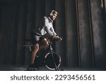 Side view of bearded man in sportswear doing exercise on bicycle simulator and listening to music in wireless headphones during workout in gym