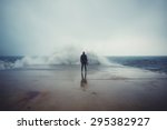 Back view portrait of young man standing against the sea on a large concrete pier with big wave beating with splash in a cloudy storm weather, feeling of freedom, male person enjoying rainy day alone