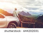 Small photo of Dreaming man traveler is enjoying freedom and fantastic jungle view, while is sitting on a car hood in summer evening. Young male tourist is admiring amazing landscape, during road trip on cuv in Asia