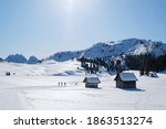 Beautiful winter mountain landscape with wooden snowy barns, cross-country ski tracks and silhouette of running skiers. Piazza Prato plateau, Sexten Dolomites, South Tyrol, Italy
