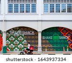 Small photo of SINGAPORE – 5 JAN 2020 – A young Asian Chinese Zeek delivery driver drives an electric scooter past a Shake Shack restaurant in downtown Singapore