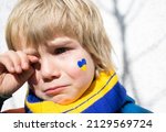 face of a frightened boy, a painted heart on the cheek in yellow-blue colors of the Ukrainian flag. Russia's invasion of Ukraine, a request for help to the world community. Children ask for peace