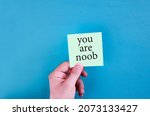 Small photo of Male hands holding a you are card note. Top view in blue background. you are noob