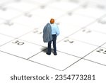 Miniature tiny people toy figure photography. Business concept illustration. A tired businessman standing above calendar. Isolated on white background. Image photo