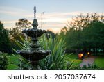 Small photo of Fountain with water drops in a park with trees behind at dusk. The fountain is seen with a path, bench and lights just after sunset. This fountain is a central feature in the park.