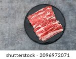 Small photo of Sliced ​​fresh raw beef. This is beef that most people in the slice call shortplate. Served on black plate on dark background. Close up.