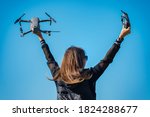 Young woman in black jacket holding remote control and drone before the flight on the blue sky background. Flying drone outside in summer.