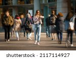 Young woman walking in the middle of crowded street and looking time at hand watches. Big city life.