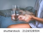 Small photo of Woman holding glass of water in shaky hands and suffering from Parkinson's disease symptoms or essential tremor.