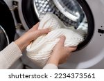 Woman putting white clothes into the drum of a washing machine, front view. Washing dirty clothes in the washer