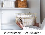 Small photo of Woman organizing clothes on shelves in white opened wardrobe, folding laundry in baskets. Space organization and storage system. Tidy up closet