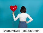 mock-up brunette woman stands with her back and holds a red heart-shaped balloon, depersonalization, isolated on a blue background .