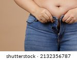 Small photo of Closeup of obese woman with overweighted stomach zipping up jeans. Sudden weight gain. Visceral fat. Body positive. Tight little clothes. Need for wardrobe change.