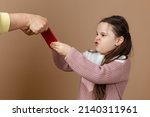 Small photo of Portrait of parent taking smartphone out from girls hands, beige background. Discontent daughter hold tight phone and oppose. Concept of prevention of telephone addiction in children, nomophobia.