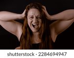 Small photo of Young angry woman rending long hair. Female portrait isolated on black. Shouting and screaming loud with open mouth. Feelings, fury, suffering. Human emotions, facial expression concept.