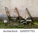 Small photo of Old rotten wooden shelves relented under the weight of kitchenware overgrown with grass and lianas. Canteen dishes in an old abandoned factory. - Image