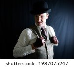 Small photo of Portrait of Man in Bowler Hat and Tweed Vest With a Mean Expression on Black Background. Old-Fashioned Ruffian or Rogue. Uncouth Cad and Notorious Criminal