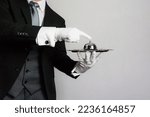 Small photo of Portrait of Butler or Concierge in Formal Attire and White Gloves Holding Bell on Silver Serving Tray. Service Industry and Professional Hospitality.