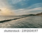 Small photo of A beach with a breakwater made of large stone boulders. View of the sea breakwater made of stones. Seascape at sunset under a cloudy sky. Waves on the sea and dark clouds in the blue sky.