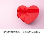 Red gift box heart-shaped on light pink table. Romantic background for Valentine Day or Birthday. Top view. Space for text. 