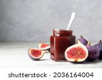 Fig jam in a glass jar on a light gray table. Fruit canning and storage. Jam for cheese and bruschetta. Space for text